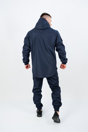 A man stands confidently in a wellfitted dark blue outdoor outfit, which includes a stylish hooded jacket and matching pants, wellsuited for any outdoor adventure in natureの写真素材