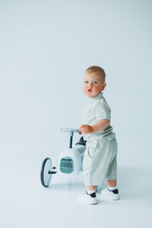 A charming toddler in a cute outfit joyfully plays on a small white tricycle, creating delightful moments in a bright, minimalistic studio filled with happinessの写真素材