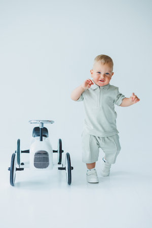 Stylish one-year-old boy in a suit with shorts and a T-shirt rides a car. Toddler boy on a white background with a toy car.の写真素材