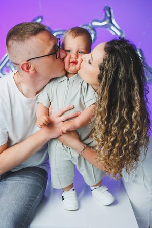 Young mom and dad on a white background playing with their one-year-old son. Toddler boy and mom and dad laughing hugging. Happy mom dad with child.の写真素材