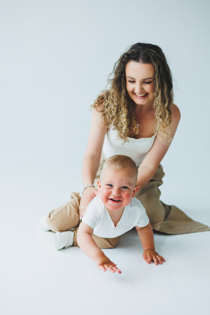 Young mother on a white background playing with her one-year-old son. Toddler boy and mother laughing hugging. Happy mother with child.の写真素材