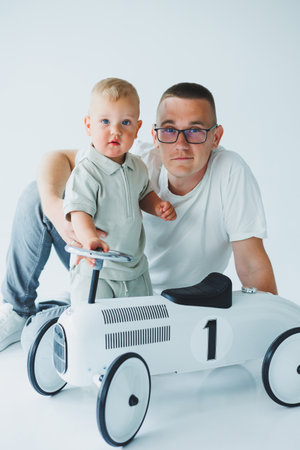 A loving father and his young child joyfully share a playful moment together with a stylish vintage rideon car in a bright, cheerful studio setting filled with warmthの写真素材