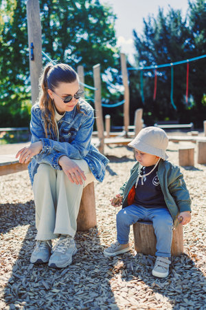 A loving moment is joyfully shared between a devoted mother and her child at a vibrant playground, radiating happiness and a deep connection under the bright sunshineの写真素材