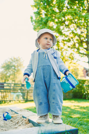 Toddler playing with a shovel in the sandbox on the playground. Boy playing in nature. 2 year old boy enjoying green grass in the park on a sunny summer day.の写真素材