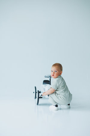 In a welllit and vivid studio, a cheerful toddler joyously crouches next to a colorful toy car, perfectly set up to capture those wonderful, joyful family and childhood momentsの写真素材