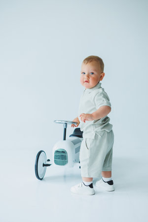 Stylish one-year-old boy in a suit with shorts and a T-shirt rides a car. Toddler boy on a white background with a toy car.の写真素材