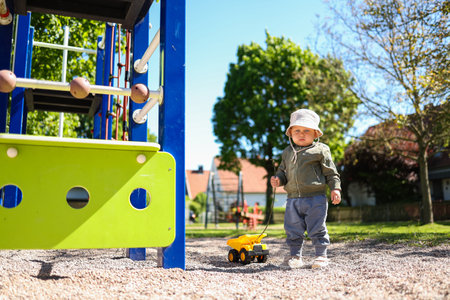Toddler boy playing on the playground outside with his plastic car. Cute 2 year old boy playing with a car in the yard. Child walking outdoors.の写真素材