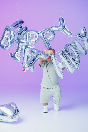 In a festive atmosphere, a cheerful toddler joyfully holds bright silver Happy Birthday balloons, making the celebration unforgettable for everyone and capturing the days joyの写真素材