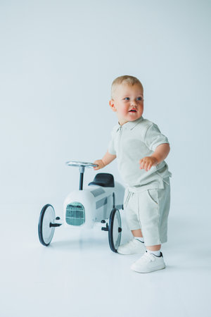 Stylish one-year-old boy in a suit with shorts and a T-shirt rides a car. Toddler boy on a white background with a toy car.の写真素材