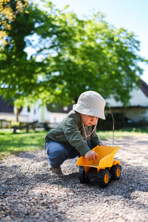 Toddler boy playing on the playground outside with his plastic car. Cute 2 year old boy playing with a car in the yard. Child walking outdoors.の写真素材