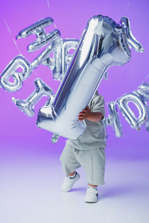 A joyful child, with a big silver number one balloon in hand, is celebrating their very first birthday party surrounded by bright, colorful decorations and cheerful vibesの写真素材