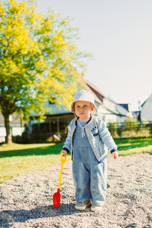 Toddler playing with a shovel in the sandbox on the playground. Boy playing in nature. 2 year old boy enjoying green grass in the park on a sunny summer day.の写真素材