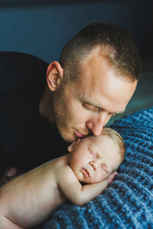 A devoted and loving father gently kisses his peacefully sleeping newborn child, showcasing the deep and beautiful bond they share in a cozy and warm setting filled with loveの写真素材