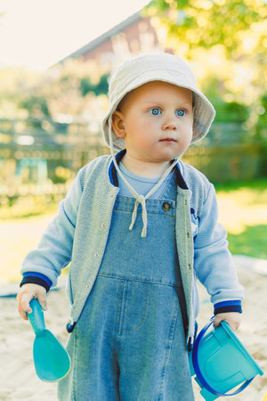 Toddler playing with a shovel in the sandbox on the playground. Boy playing in nature. 2 year old boy enjoying green grass in the park on a sunny summer day.の写真素材