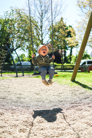 2 year old boy in a Panama hat on his head and a light jacket swings on a swing. Children's swing on...
