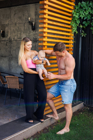 A young couple enjoys a warm moment in nature, with the mother holding their baby and the father playfully interacting, showcasing genuine family love and memoriesの写真素材
