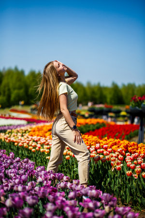 A young woman is relishing a wonderfully sunny day while surrounded by vibrant, blooming tulips, skillfully capturing the essence of spring in a truly picturesque floral landscapeの写真素材
