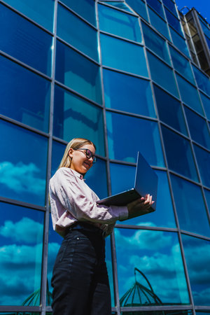A confident woman exudes positivity and determination, smiling while working on her laptop outdoors, embodying productivity and empowerment in a vibrant urban settingの写真素材
