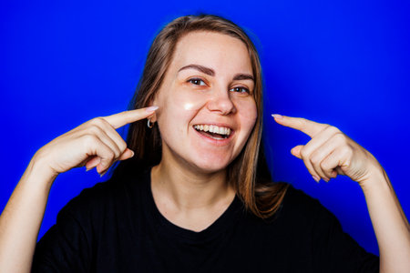 A cheerful young woman with a radiant smile poses against a vibrant blue background, embodying joy...