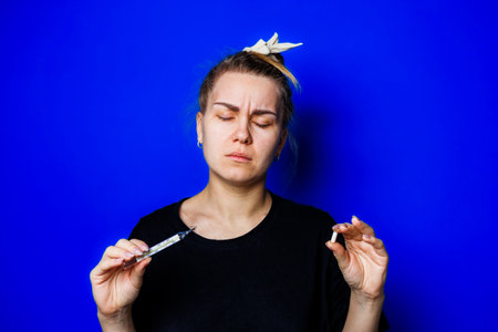 A woman with a syringe in one hand and a cigarette in the other symbolizes inner conflict, set against a bold blue backdrop, reflecting lifes emotional strugglesの写真素材
