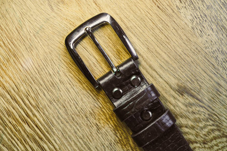 A detailed view of a classic brown leather belt featuring a sturdy metal buckle, laid against a rustic wooden surface. Perfect for fashion and accessories shoots.の写真素材