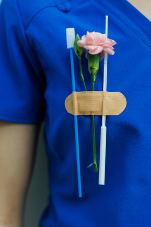 The image features a striking blue uniform next to dental tools, beautifully complemented by a vibrant pink flower, merging healthcare with artistic expressionの写真素材