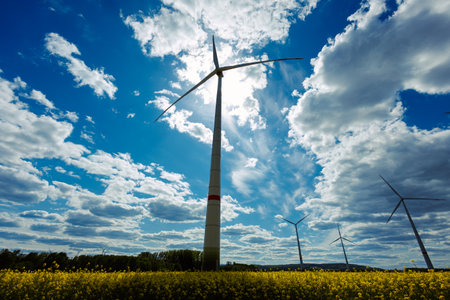 A field of wind turbines generating energy standing in a green field. Wind turbines in a yellow field somewhere in the countryside in Europe.の写真素材