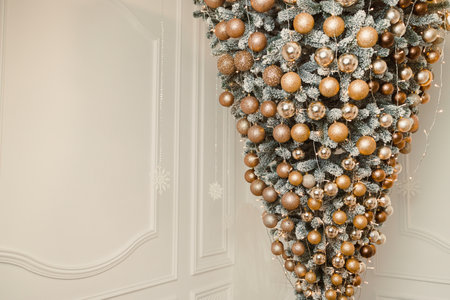 A breathtaking upsidedown Christmas tree, beautifully adorned with shimmering gold and silver ornaments, brings a distinctive festive charm to a chic and modern interior spaceの写真素材