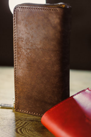 A brown leather wallet, expertly crafted, rests on a wooden table beside a vibrant red wallet,...