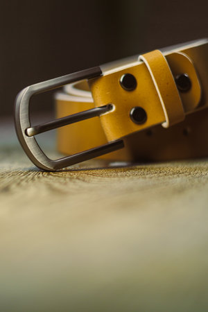A closeup of a stylish yellow leather belt with a sleek metal buckle on a rustic wooden surface, highlighting its exquisite style and highquality craftsmanshipの写真素材