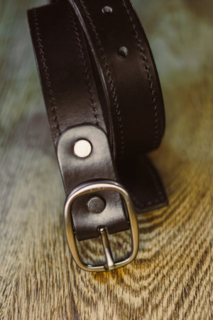 The closeup image shows a sleek black leather belt with a shiny silver buckle on a rustic wooden surface, appealing to fashion enthusiasts and accessory loversの写真素材