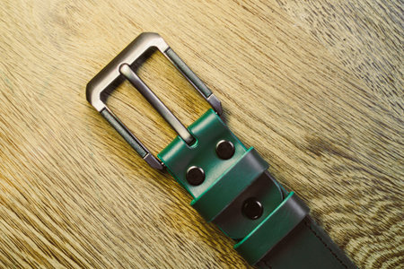 A chic and stylish green leather belt that features a slim metallic buckle, showcasing its elegant design beautifully set against a textured wooden surface for added visual appealの写真素材