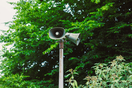 A tall outdoor speaker, securely mounted on a sturdy pole, is strategically placed amid the vibrant green trees, making it perfect for public announcements or community eventsの写真素材
