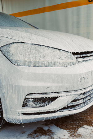 A pristine snowwhite vehicle at a bustling car wash, coated in foamy suds, exhibits an impressive and brilliant shine that captures the attention of everyone strolling byの写真素材