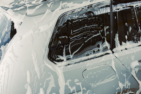 This image shows a closeup of a car being washed, with dense soap foam covering the window and body, highlighting the meticulous cleaning for vehicle maintenanceの写真素材