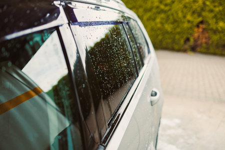 Raindrops fall on the car window, reflecting the vibrant greenery of trees and charming cobblestone streets, capturing a blissful moment of tranquility and peaceの写真素材