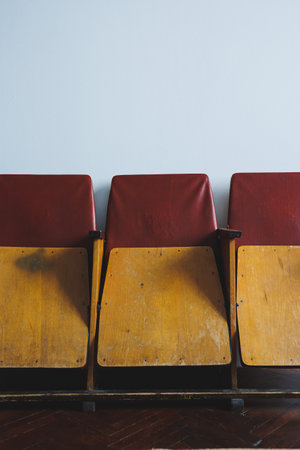 Closeup of three vintage wooden theater chairs with red upholstery, highlighting a retro aesthetic against a simple wall, perfect for adding character to any spaceの写真素材