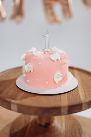 This charming pink cake, beautifully adorned with delicate flowers and topped with a vibrant candle, is absolutely perfect for celebrating a joyous childs first birthday partyの写真素材