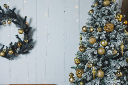 A beautifully decorated Christmas tree with golden ornaments and a frosted finish, paired with a matching wreath, creating a cozy holiday ambiance filled with warmthの写真素材