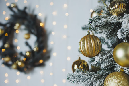 A beautifully decorated Christmas tree, adorned with golden ornaments, stands against a twinkling backdrop of colorful lights, complemented by a festive wreathの写真素材