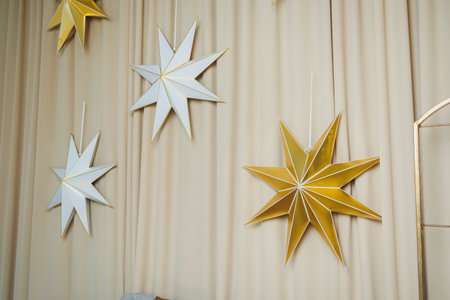 Elegant white and gold paper stars, suspended against a warm background, enhance holiday decorations, creating an enchanting atmosphere everyone will appreciateの写真素材