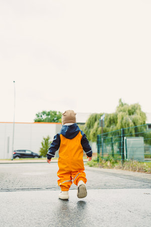 A child in a bright yellow rain suit strolls along a wet pathway, showcasing their adventurous...