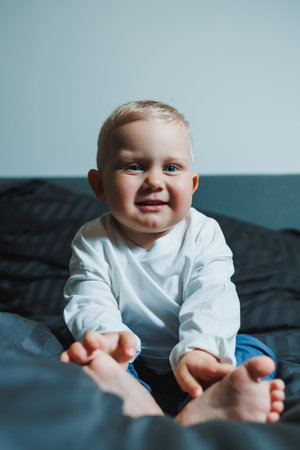 The baby smiles warmly on a cozy bed, radiating happiness and innocence, capturing joyful childhood...