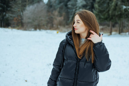 A young woman with curly hair, in a chic black jacket, stands confidently in a snowy field, celebrating winter fashion and natures beauty in an adventurous landscapeの写真素材