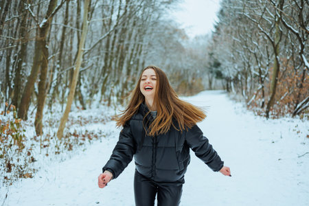 A cheerful young girl with curly hair enjoys a delightful and snowy winter day, joyfully running down a peaceful forest path surrounded by beautiful snowcovered treesの写真素材