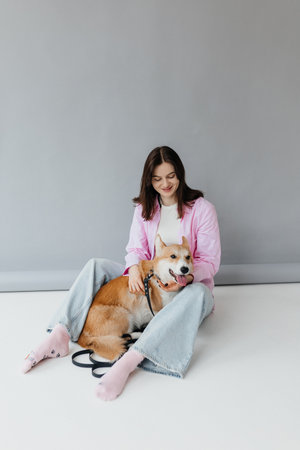 Cute brunette woman in white t-shirt and jeans hugging corgi puppy on white background. Love for animals, pets concept. cheerful woman holding welsh corgi dog.の写真素材