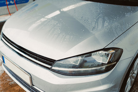 A sleek silver car hood glistens with water droplets after a thorough wash, showcasing the shiny surface and well-designed headlights. Perfect for automotive imagery.の写真素材
