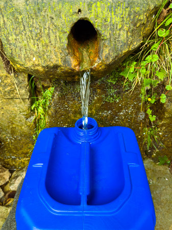 Fresh water flows from a spring into a blue container, emphasizing the need for sustainable water...