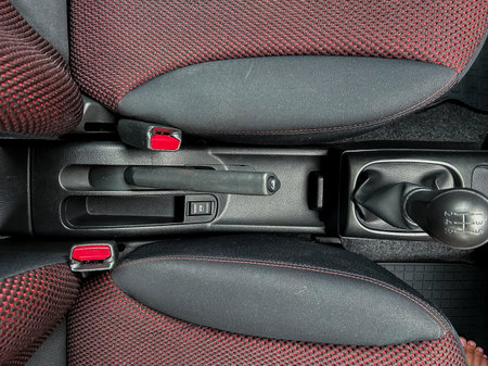 An aerial view of a cars console with textured upholstery, a gear shift, and complex seat...