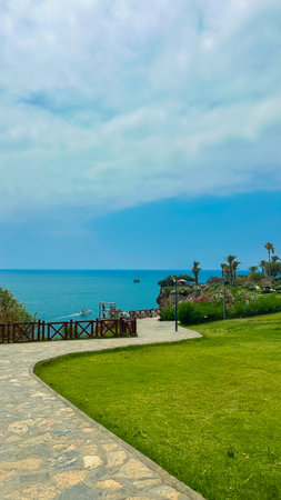 Imagine a stunning coastal view with clear waters, vibrant green laws, and a winding pathway leading...